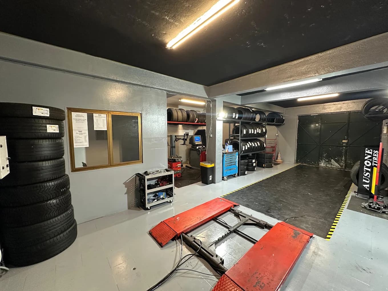 Interior da oficina Frisos Pneus com pneus em stock, equipamento de montagem e elevador